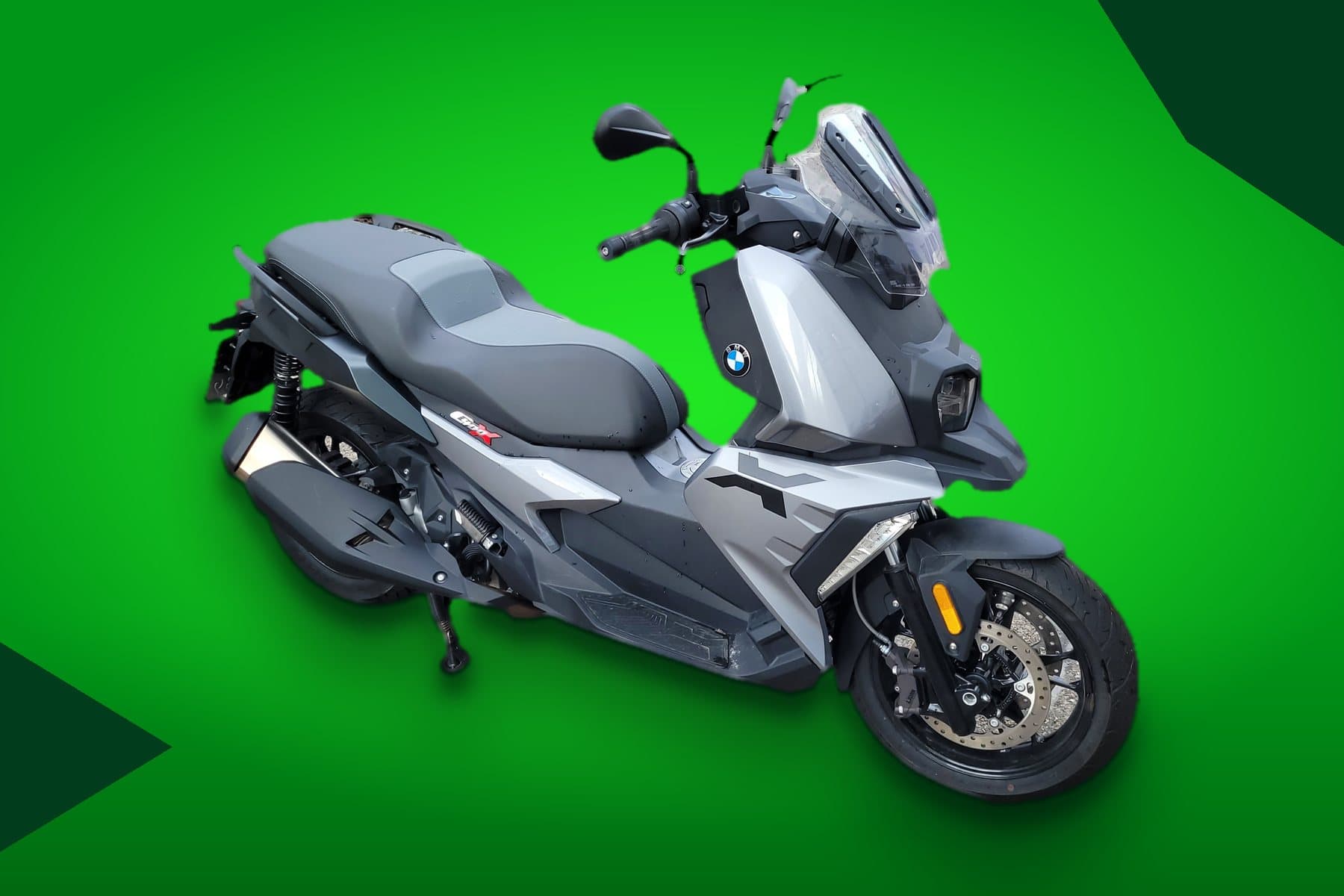 Scooter BMW C 400 X cinza e prata, vista de frente e de lado, com o emblema BMW na carenagem, em fundo verde Stone